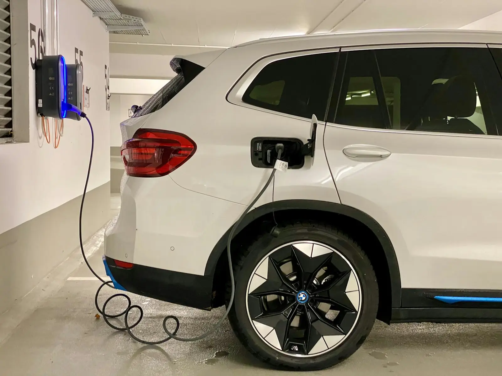 Voiture électrique blanche branchée à une wallbox murale installée par Voltéo