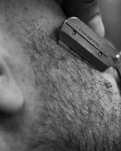 Rasoir qui trace le contour d’une barbe près de l’oreille, en noir et blanc