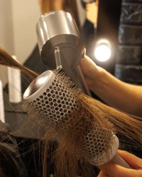 Brosse ronde et sèche-cheveux qui lissent une longueur châtain