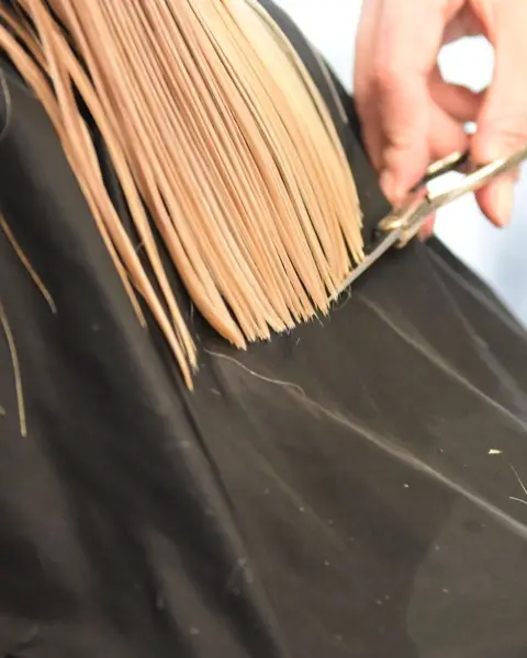 Ciseaux qui coupent droit une longueur blonde au-dessus d’une cape noire