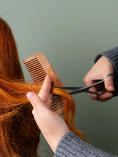 Mains qui coupent une mèche de cheveux roux entre peigne et ciseaux