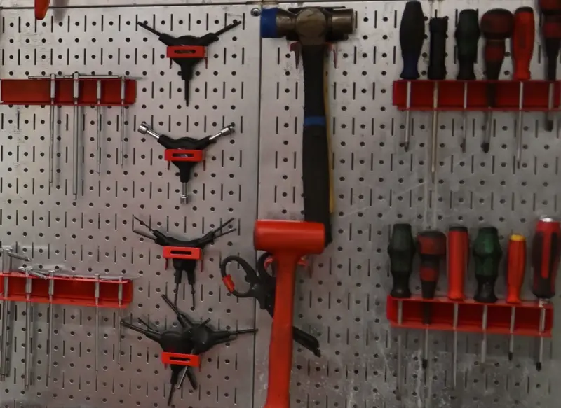 Panneau perforé en tôle galvanisée : clés à rayons, clés en Y, clés six pans, marteau et tournevis rangés sur des supports rouges