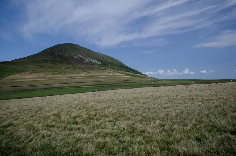 Le puy de l’Angle, volcan couvert d’herbe, au-dessus d’une prairie de fauche sous un ciel bleu