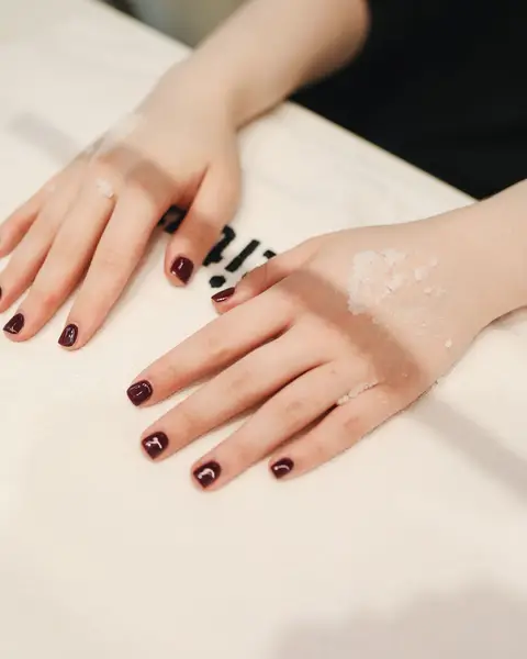Deux mains à plat sur une serviette, ongles très courts vernis bordeaux