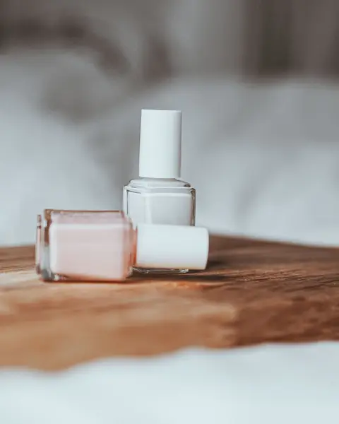 Deux flacons de vernis rose pâle et blanc laiteux sur un plateau en bois