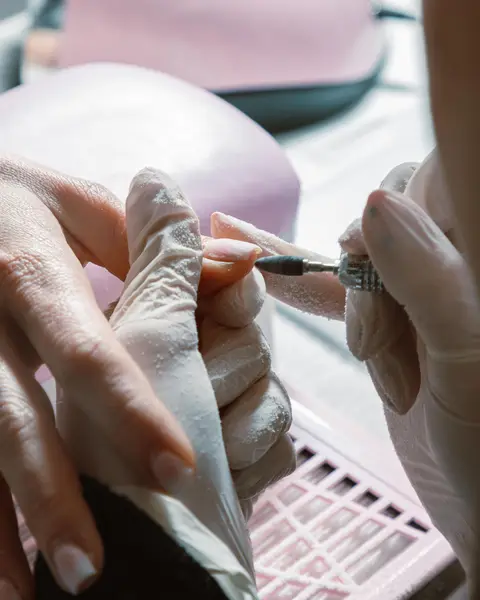 Praticienne gantée qui lime un ongle en gel devant la lampe de séchage
