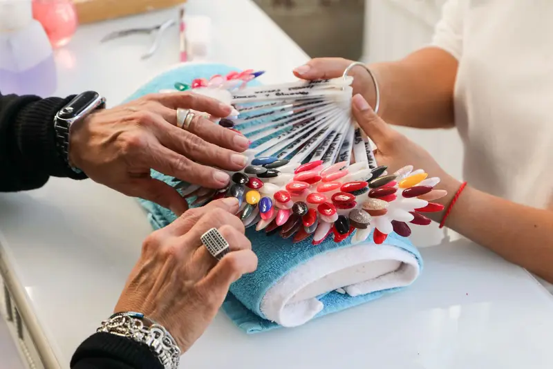 Deux mains passent en revue un nuancier en éventail de faux ongles vernis, posé sur une serviette au comptoir