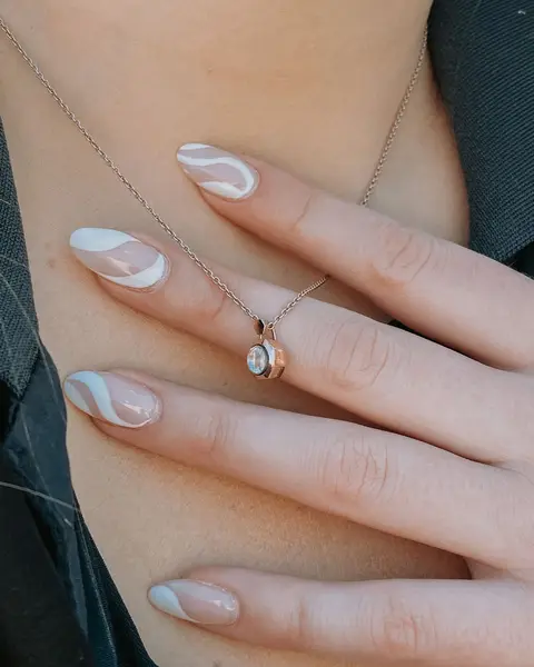 Ongles en amande nude rosé, traversés d’une volute blanche, main posée sur une épaule