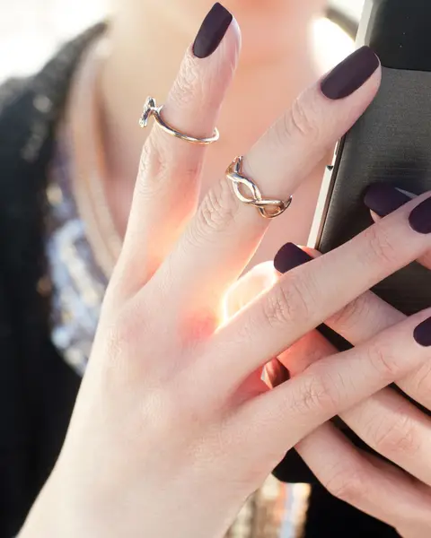 Main aux ongles en amande vernis prune mat, bagues fines aux doigts