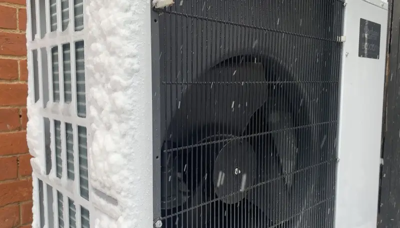 Pompe à chaleur en fonctionnement sous la neige, givre sur les ailettes