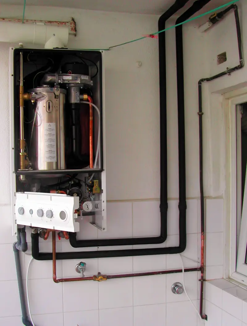 Chaudière murale gaz ouverte, capot retiré : corps de chauffe, tuyaux de cuivre, manomètre et robinet d’arrivée de gaz