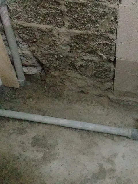Salle de bains déposée jusqu’au mur de parpaings : un tuyau d’arrivée d’eau le long du mur, le tuyau d’évacuation posé sur la chape