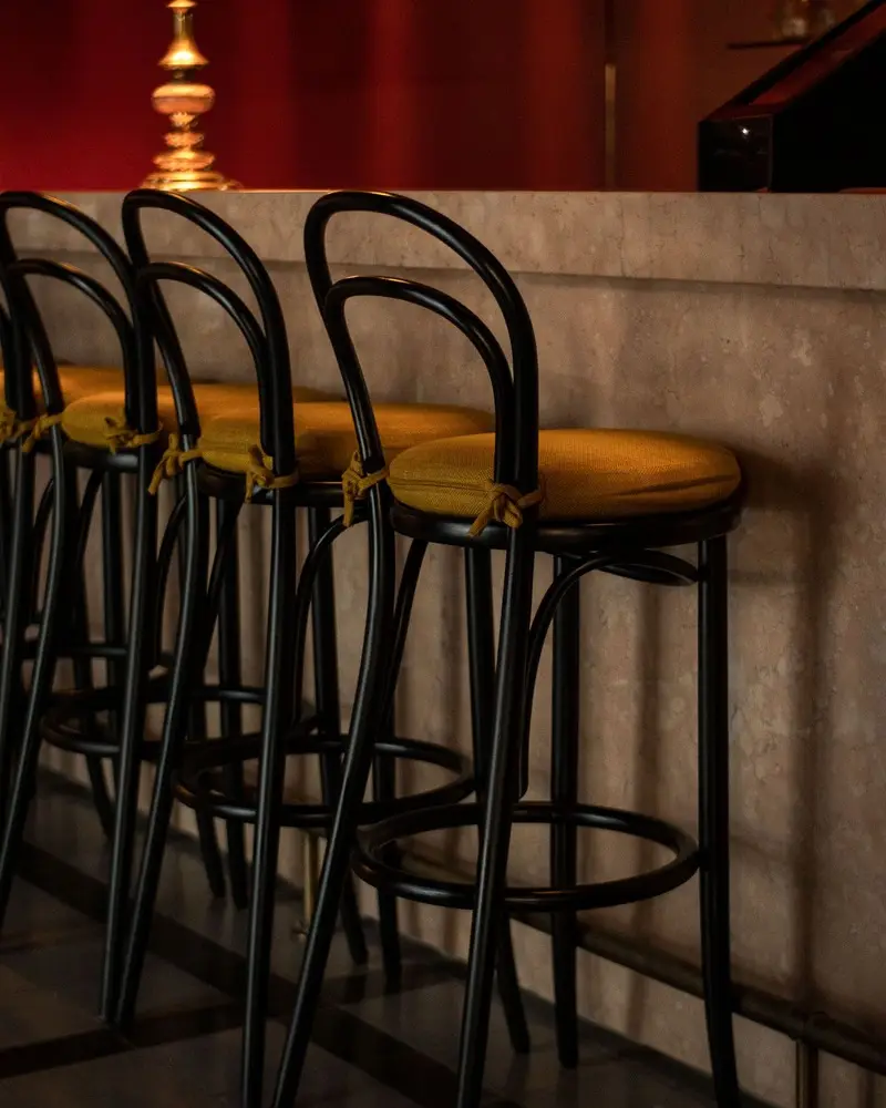 Rangée de tabourets hauts noirs à assise dorée devant un comptoir, une lampe à abat-jour posée au fond