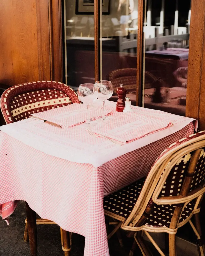 Table dressée d’une nappe à petits carreaux rouges, verres à pied, chaises en rotin