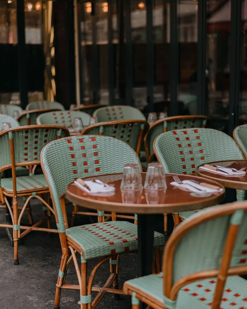 Chaises de terrasse en rotin tressé vert d’eau autour de petites tables rondes, sur le trottoir