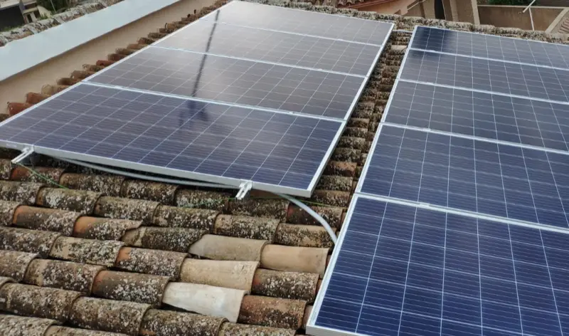 Deux rangées de panneaux photovoltaïques fixées sur rails au-dessus d’une couverture en tuiles canal couvertes de lichen
