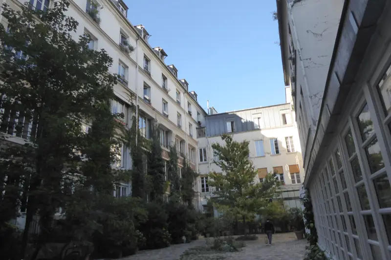 Cour pavée du faubourg Saint-Antoine, façades blanches, arbres, ancien atelier vitré sur la droite